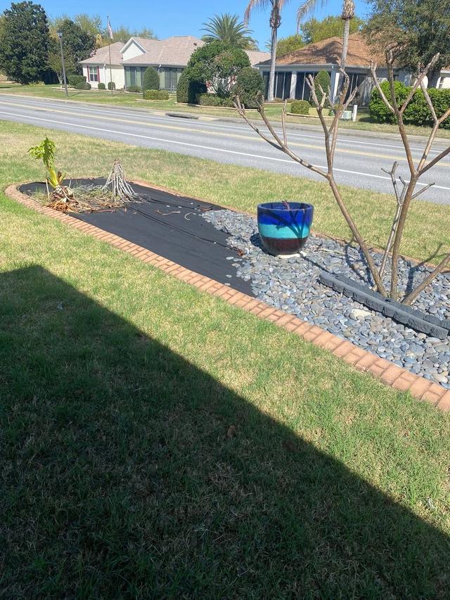 A landscape rock bed with new weed barrier laid down and river rock being set back over it, edged with brick