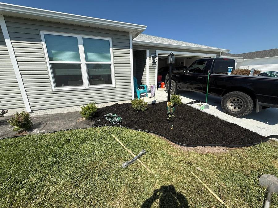 A finished mulched bed along the front of a home with the work truck still parked in the driveway